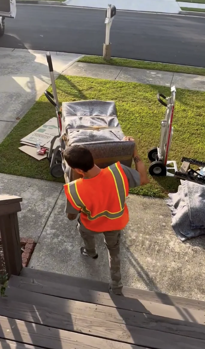 Mover carrying a wrapped sofa down front steps