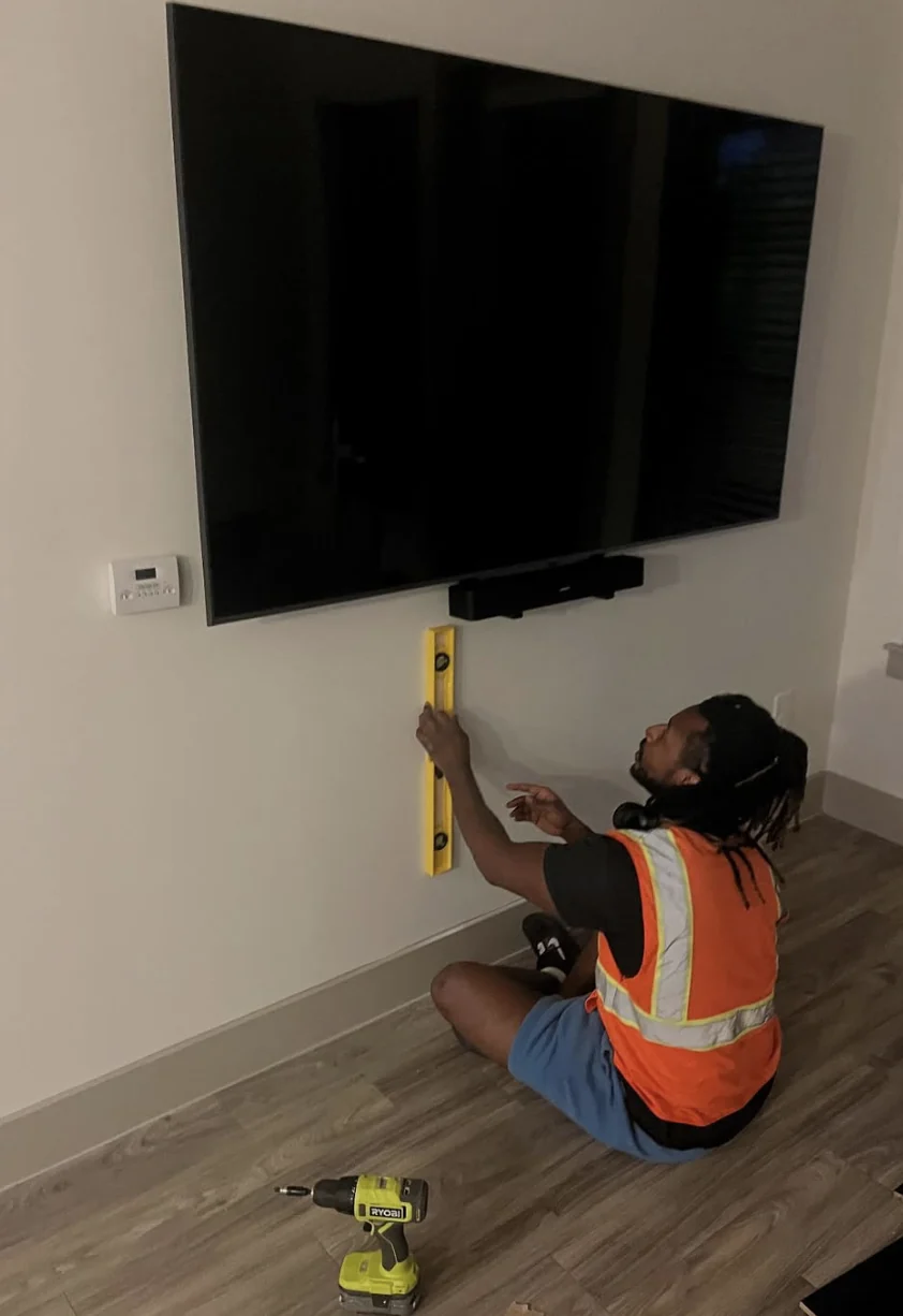 Worker checking a wall-mounted television with a level