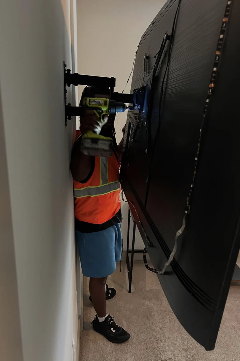 Worker fastening a wall mount behind a television